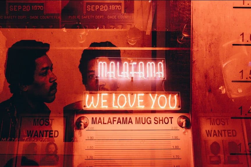 Pared de carteles MOST WANTED con los neones MALAFAMA y WE LOVE YOU
