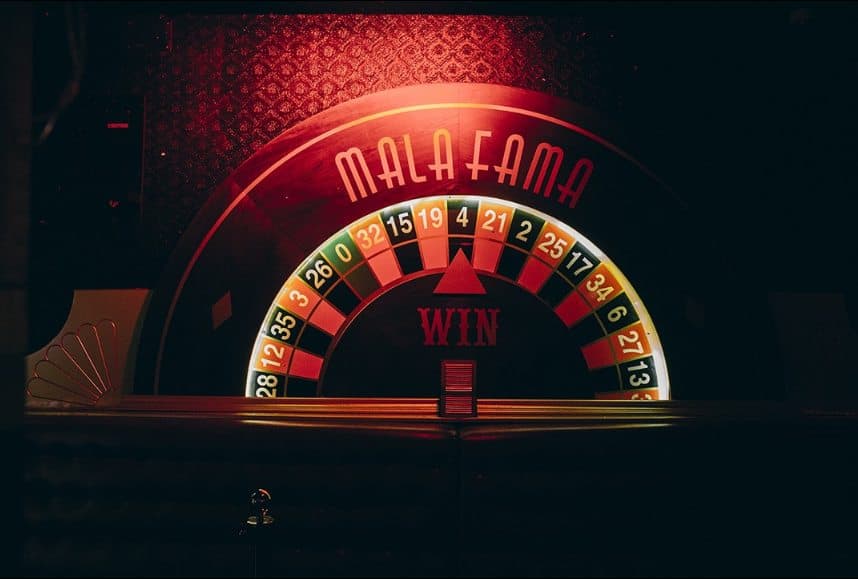 Ruleta gigante iluminada con el rótulo MALAFAMA y la palabra WIN